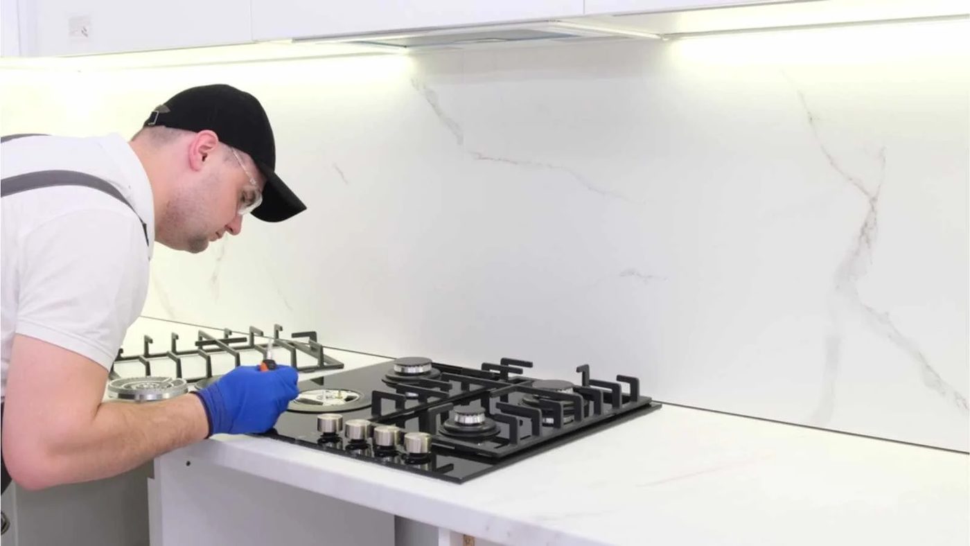 A gas engineer repairs a gas stove in the kitchen. The call of the master gas fitter to the house.