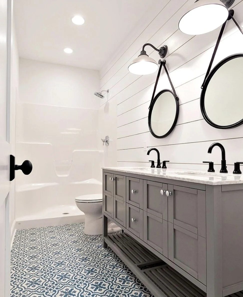 Bathroom With Shiplap White Walls, striking Blue Tiled Floor And vivid Double Sink Vanity With Two Circle Hanging Mirrors