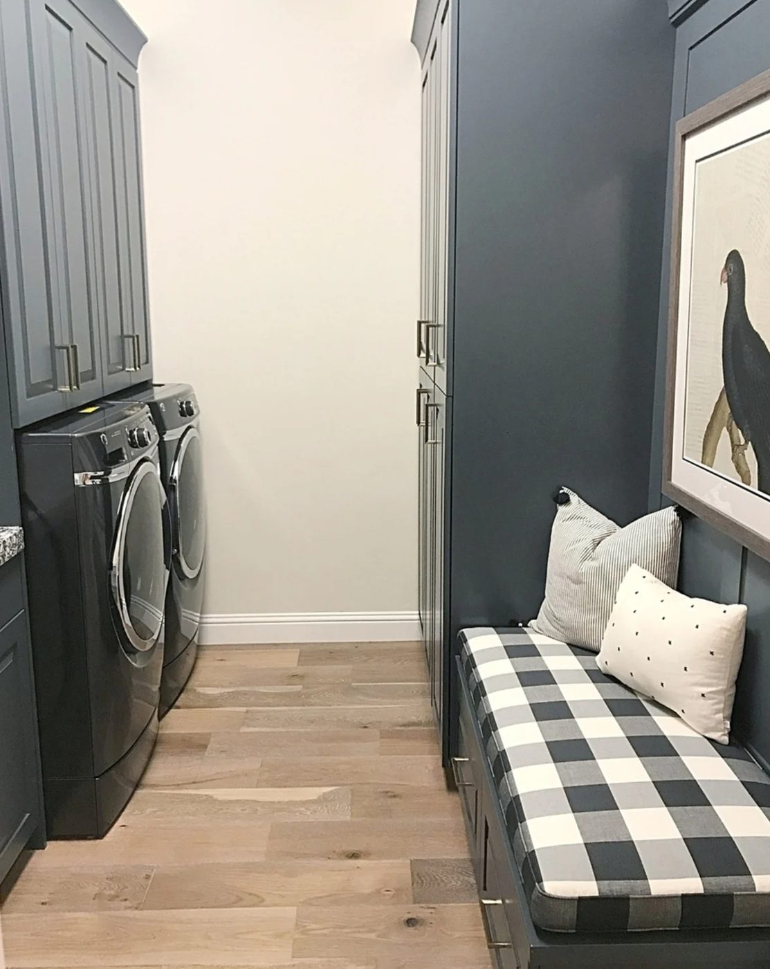 Grey Cabinets In Laundry Room With Cupboard Over Washer And Dryer And Checkered Black And White Bench With Cupboards Underneath