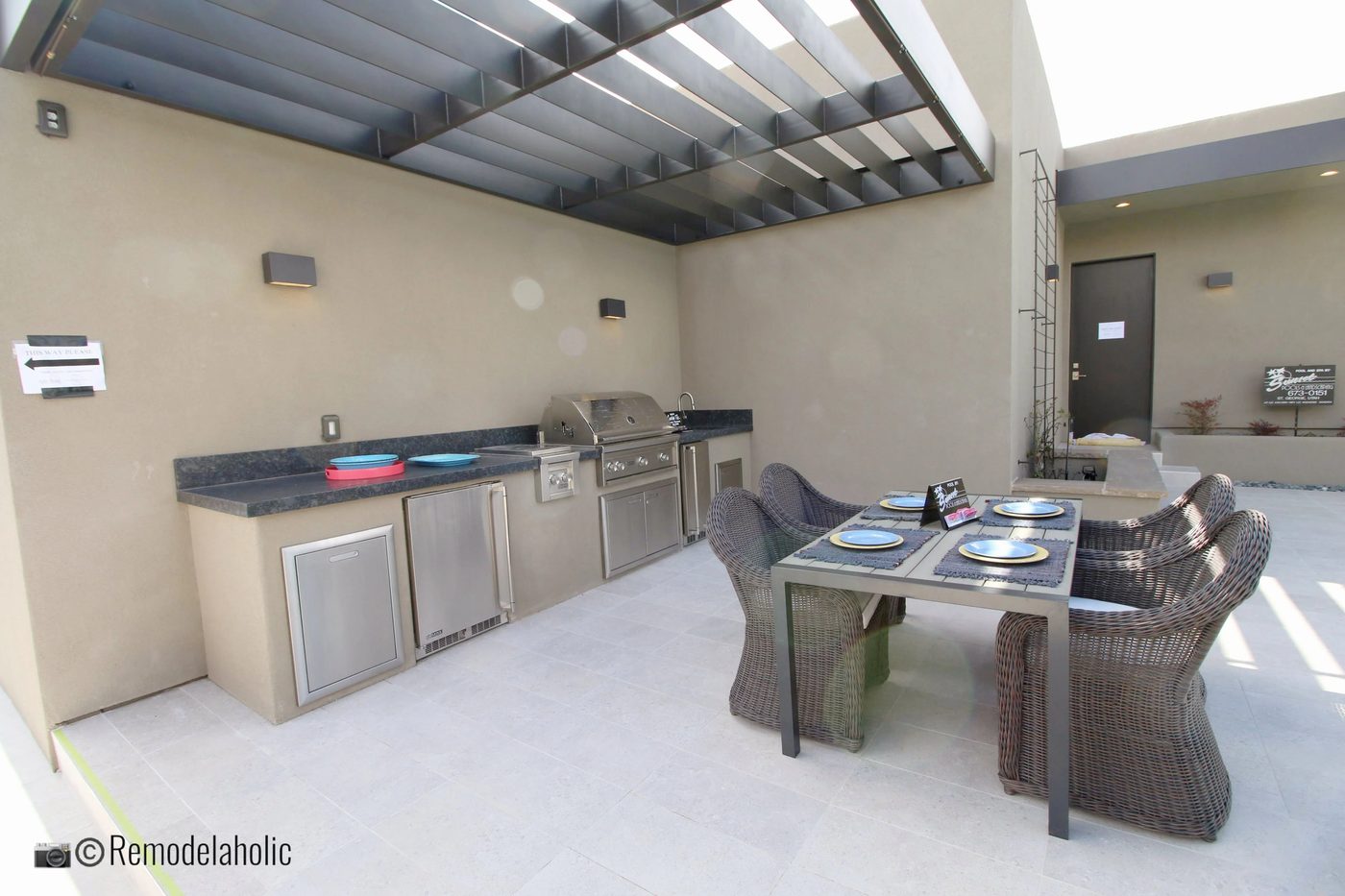 Outdoor kitchen area with patio table and wicker chairs. SGPH 2019 House 15 Split Rock Custom Homes, Photo by Bekob