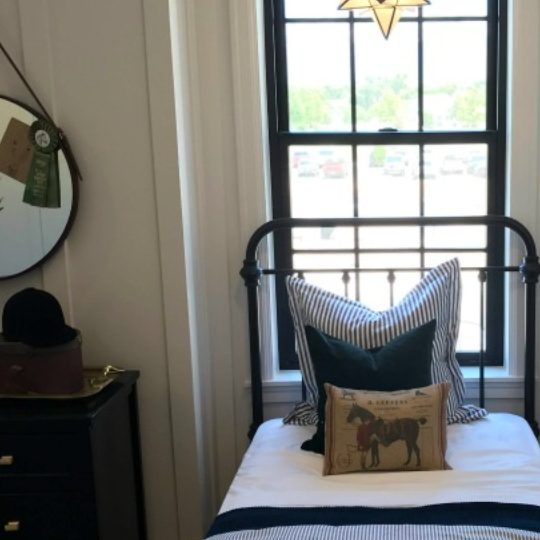 Farmhouse Themed Boys Bedroom With Metal Bedframe And Striped Bedspread And Pillow With Horse Pillow And White Accented Walls