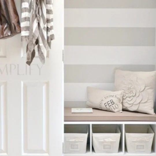 Closet With White Door Open And Blue And White Striped Accent Wall Inside, Bench, Pillows, And Baskets Underneath