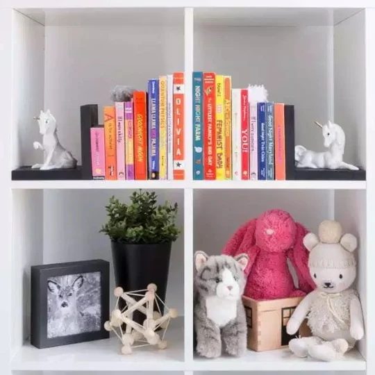 White Square Bookshelves With Colorful Children's Books And Unicorn Book Ends And Stuffed Animals, Cat Photo In Picture Frame, Plant And Wooden Star Toy