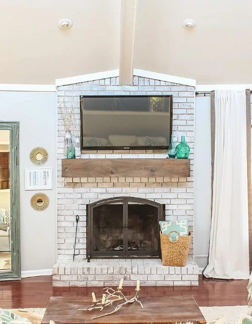 options for Decorating Around a TV Over the Fireplace Mantel, white painted brick fireplace with wood mantel via Designing Vibes