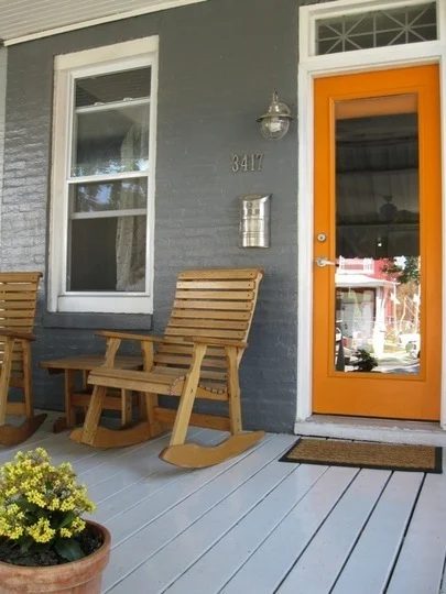 Grey Wooden Porch With Grey Painte Bricks And Orange Door With Long Glass Center And Wooden Rocking Chairs