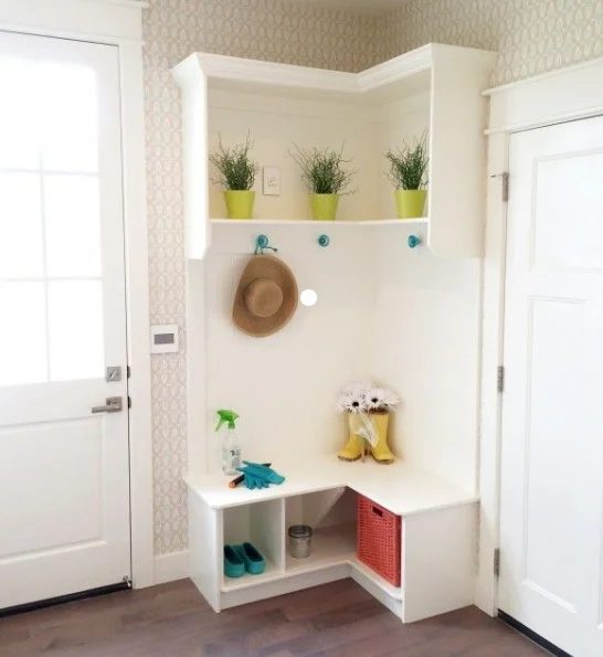 Tall White Corner Shelf With Hooks And Cubbys, Lit With Colorful Flower Pots And Greenery, Rainboots, Garden Gloves And A Wicker Basket