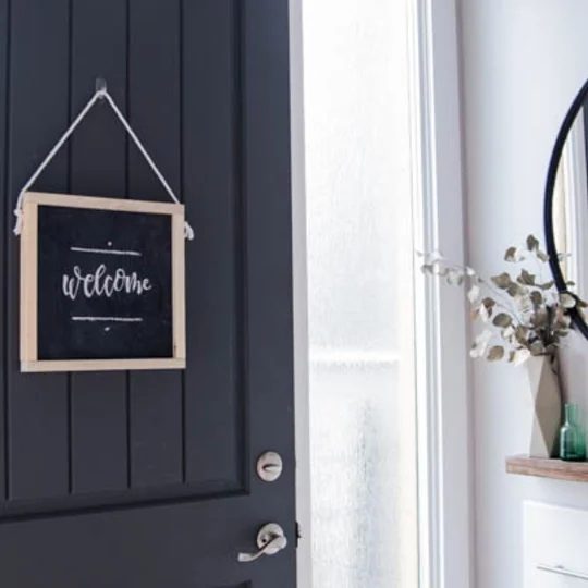 Wooden Chalkboard Sign On A Dark Front Door With White Walls