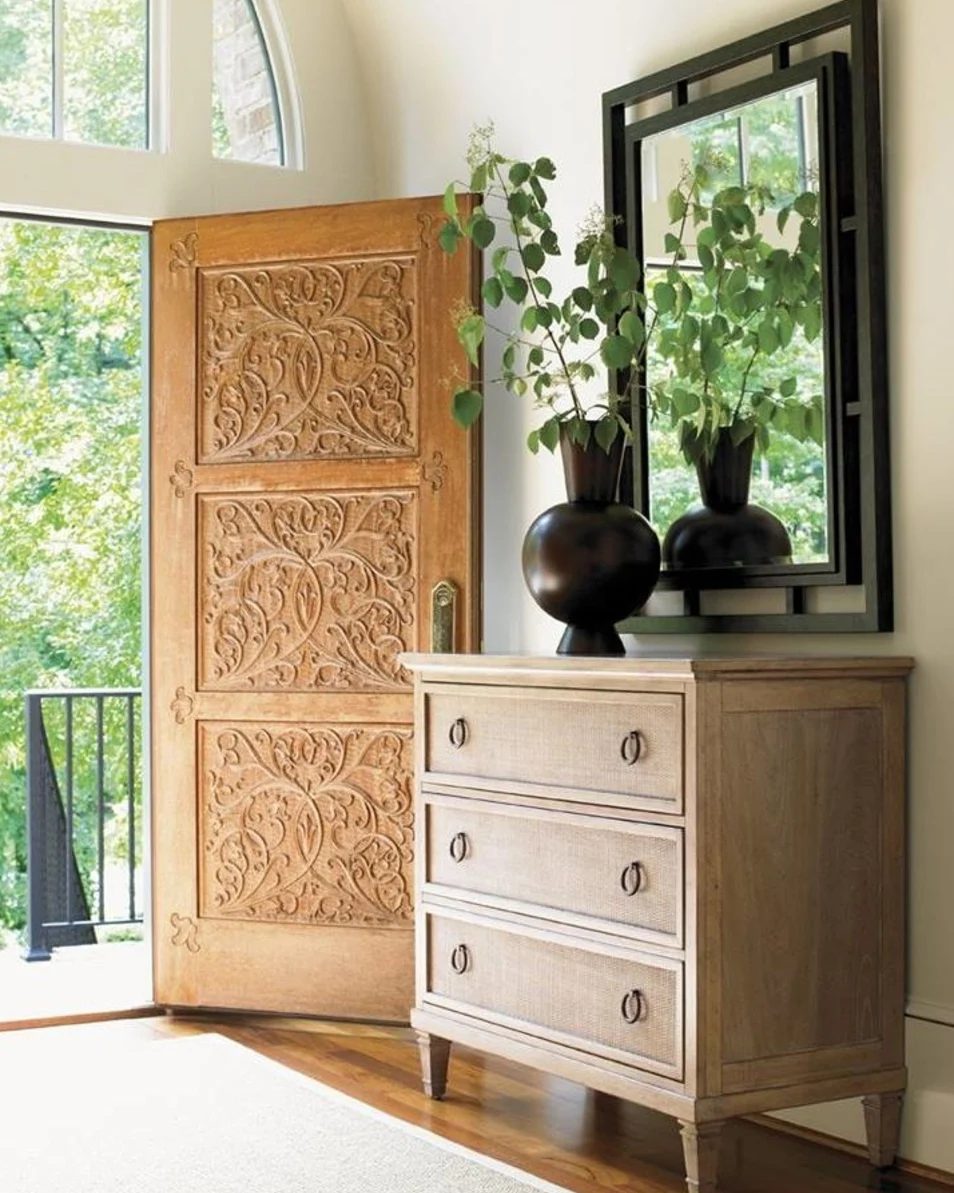 Entryway With Wooden Detailed Front Door, Wood Dresser, Black Mirror, Vase And Greenery