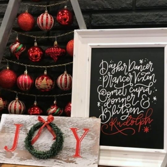 Handmade Christmas Signs, JOY Sign With Wreath As O, White Frame With Black Sheet And White Text Of Reindeer Names In Calligraphy, Ornament Christmas Tree Behind