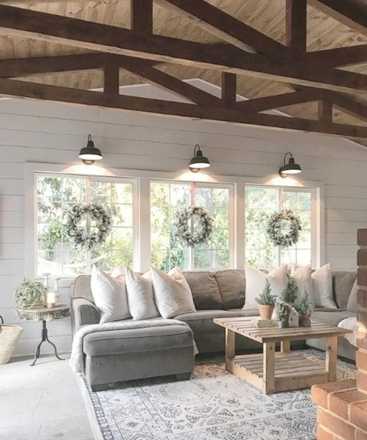Living Room With High Rise Ceilings And Wooden Beams And Open Windows With Lights Above And Wreaths And Grey Couch With White Cushions