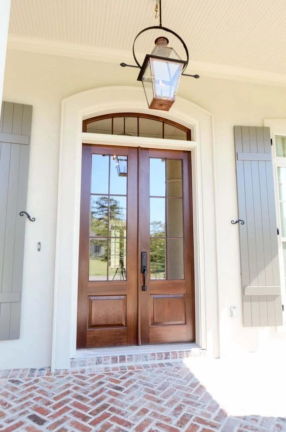 striking front entry with wood doors and transom, shutters, and brick porch - via Bevolo