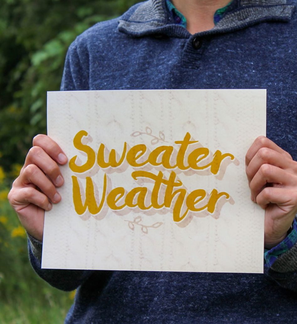 Sweater Weather Printable With Yellow Font Being Held By Someone With Blue Sweater On