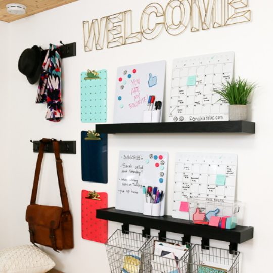 White Wall With Black FLoating Shelves And Hanging Baskets And Calendars And Clipboards And Hooks
