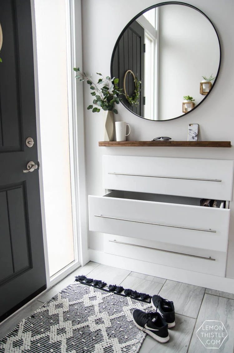 Grey And White Entryway With Drawers Into The Wall, Stainless Steel Bar Handles And Circular Mirror And Wooden Shelf