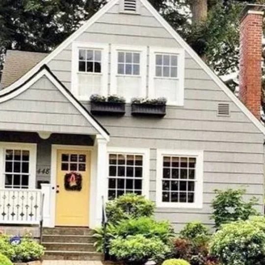 Green Home With White Trimmed Windows With Window Flower Boxes And A Yellow Front Door