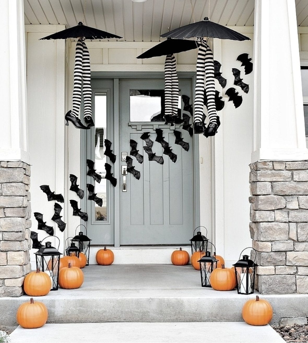 vivid Front Door With Pumpkins, Black Lanters, Plastic Bats Taped Across The Porch And Witches Legs In Striped Tights And Black Heels Under Black Umbrellas