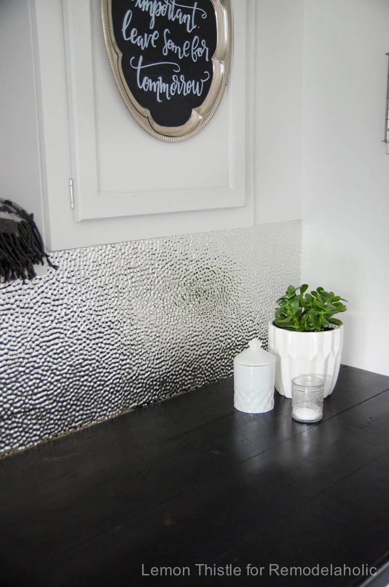 A textured metal ceiling tile backsplash is chic, modern, and durable -- and straightforward to install with a good pair of gloves and the right adhesive!
