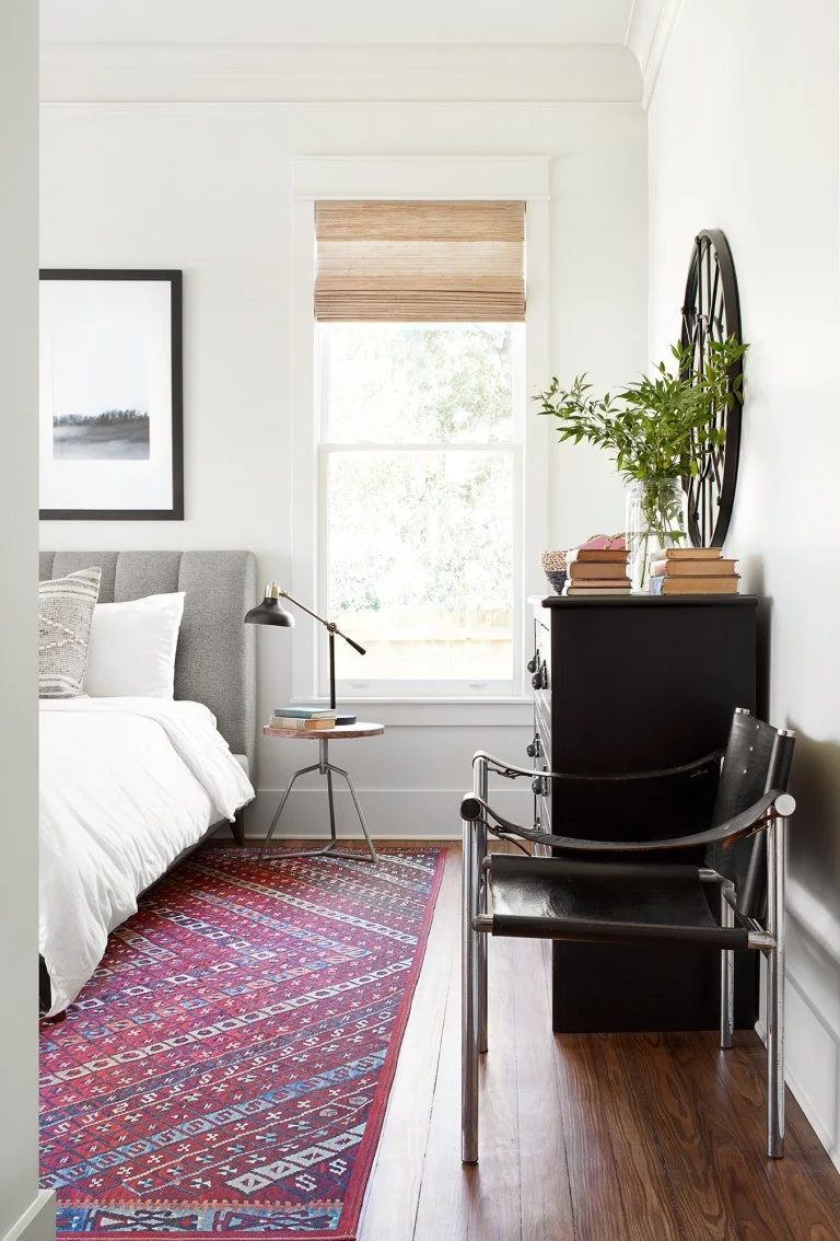 Bedroom With Red Rug, White Bedspread And Black Dresser