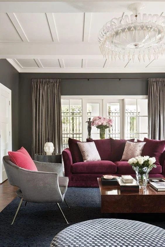 Living Room With Grey Walls, White Accented Ceiling, Chandalier, Burgundy Couch, Grey Chair And Wood Table