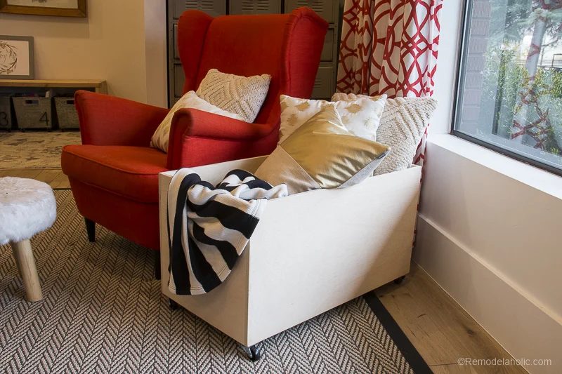 Plywood Storage Box With Wheels Filled With Pillows And Blankets Next To Arm Chair And Window
