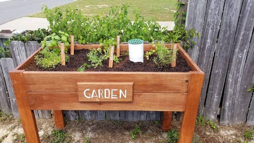 Stained Wood Box With Tall Legs With Garden Sign On The Front, Plants Inside