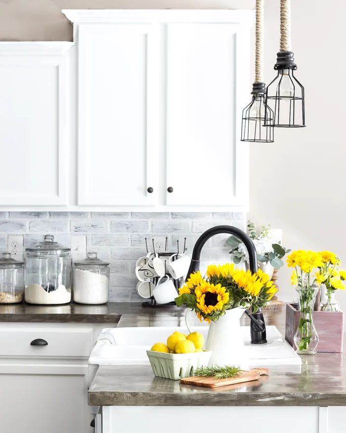 strong Light Kitchen With White Cabinets And Grey Brick Backsplash And Glass Jars And Sunflowers, And Lemons