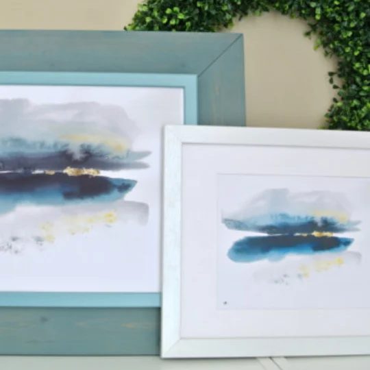 Large Turqouise Frame With Abstract Print And Smaller White Frame With Abstract Print In Front With Large Green Wreath Behind Both