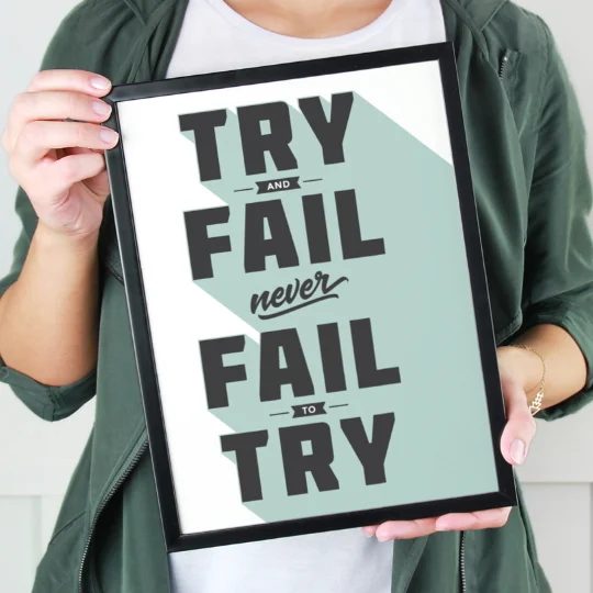 Hands Holding Black Frame With Bold Text Saying Try And Fail And Never Fail To Try With Green Sstream Behind Words