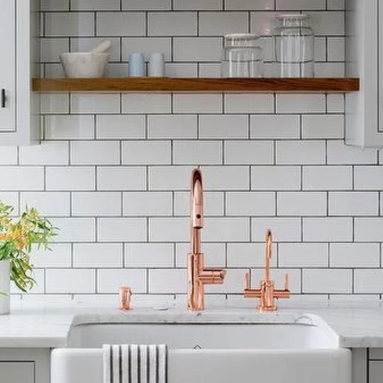 White Brick Backsplash With White Basin Sink And Gold Faucets And Wood Shelf Above