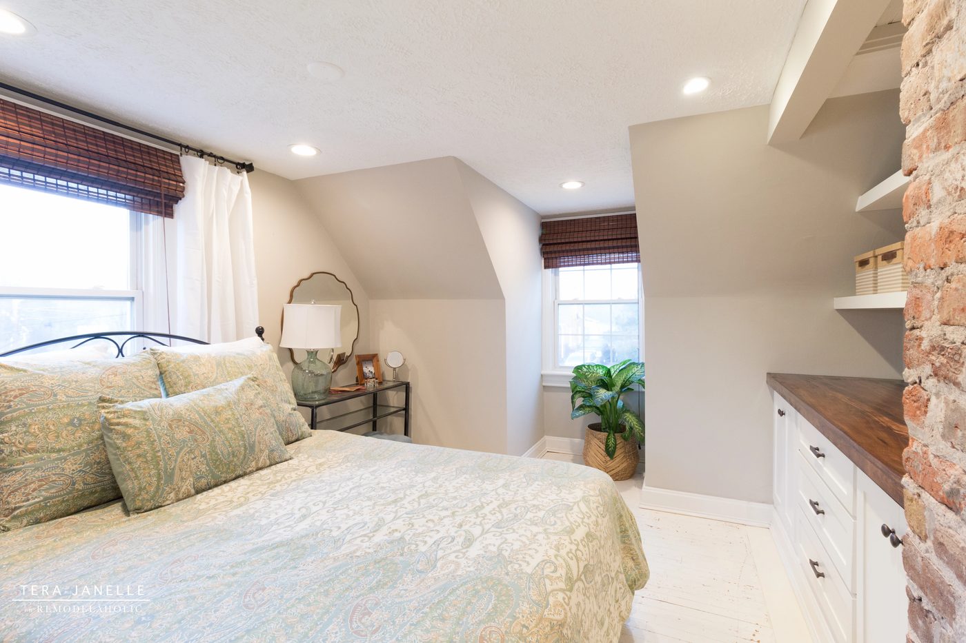 A striking travel-inspired master bedroom with an exposed brick wall and a striking built-in bookshelf and storage nook. Tera Janelle on Bekob.com