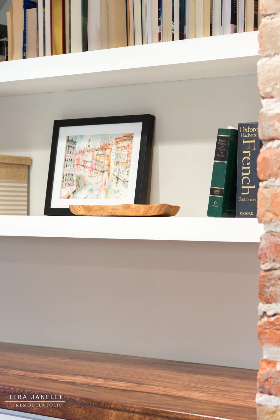 A striking travel-inspired master bedroom with an exposed brick wall and a striking built-in bookshelf and storage nook. Tera Janelle on Bekob.com