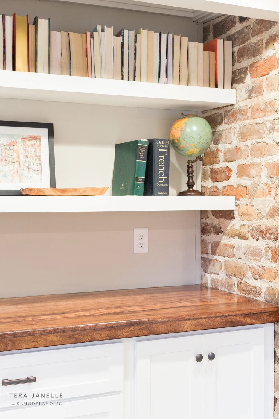 A striking travel-inspired master bedroom with an exposed brick wall and a striking built-in bookshelf and storage nook. Tera Janelle on Bekob.com