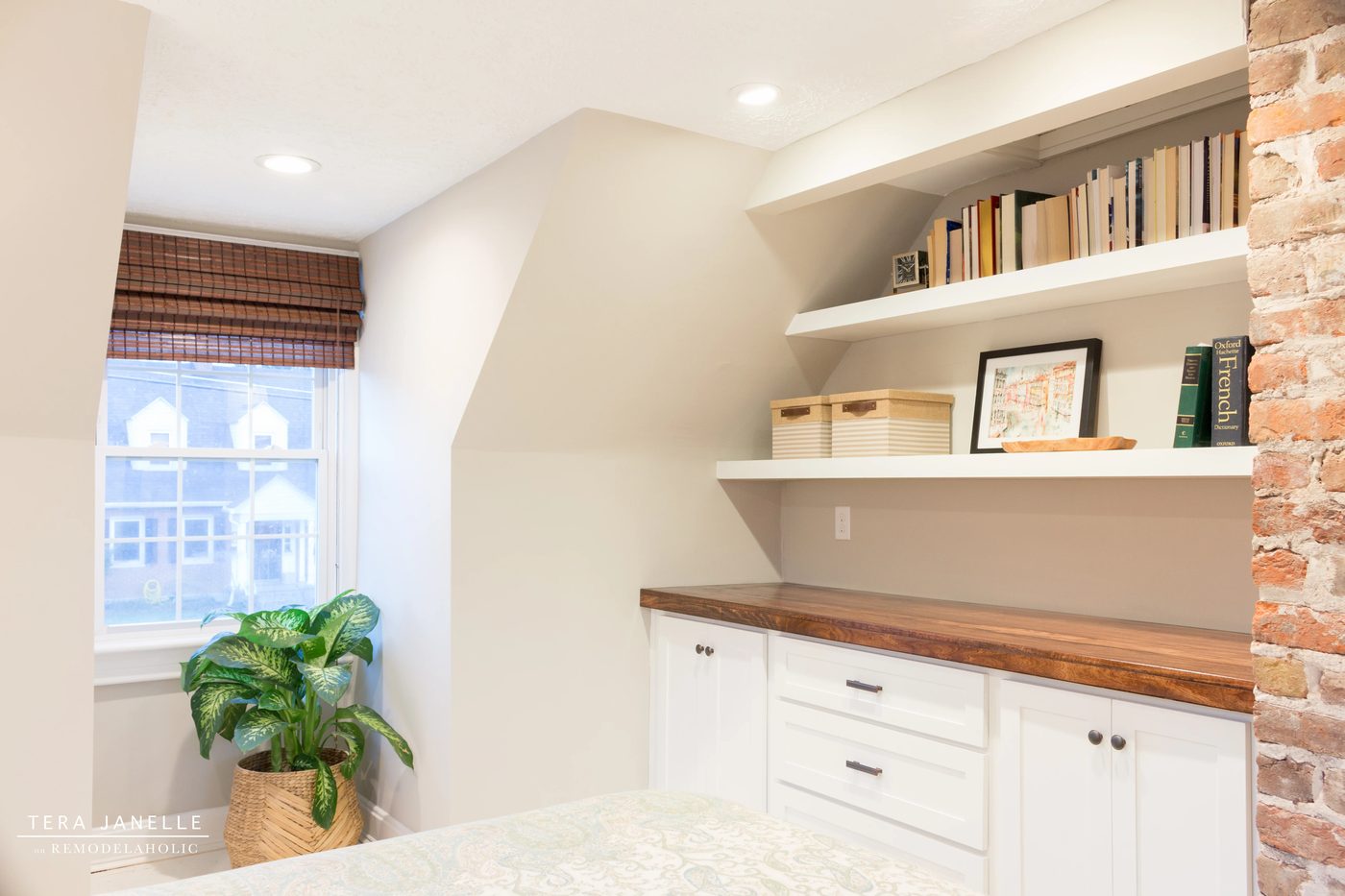 A striking travel-inspired master bedroom with an exposed brick wall and a striking built-in bookshelf and storage nook. Tera Janelle on Bekob.com