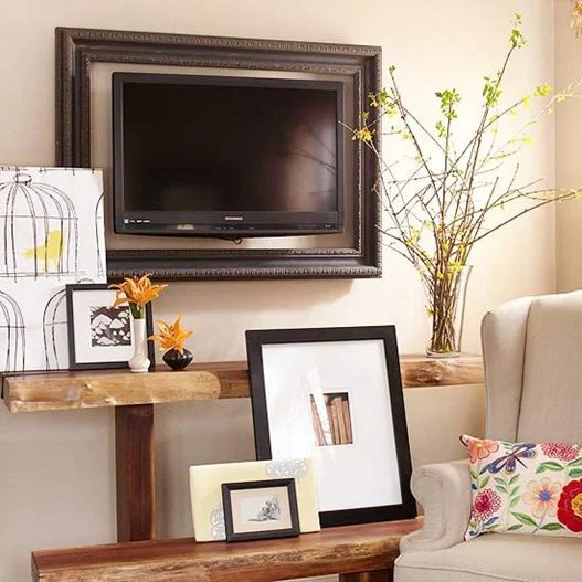 layered decor and shelving around a framed television to help it blend in (BHG)