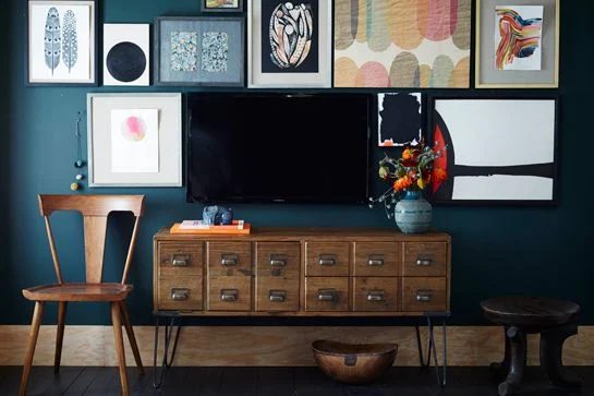 paint a dark wall behind the TV and hang a gallery wall to hide the television (West Elm via Refinery 29)
