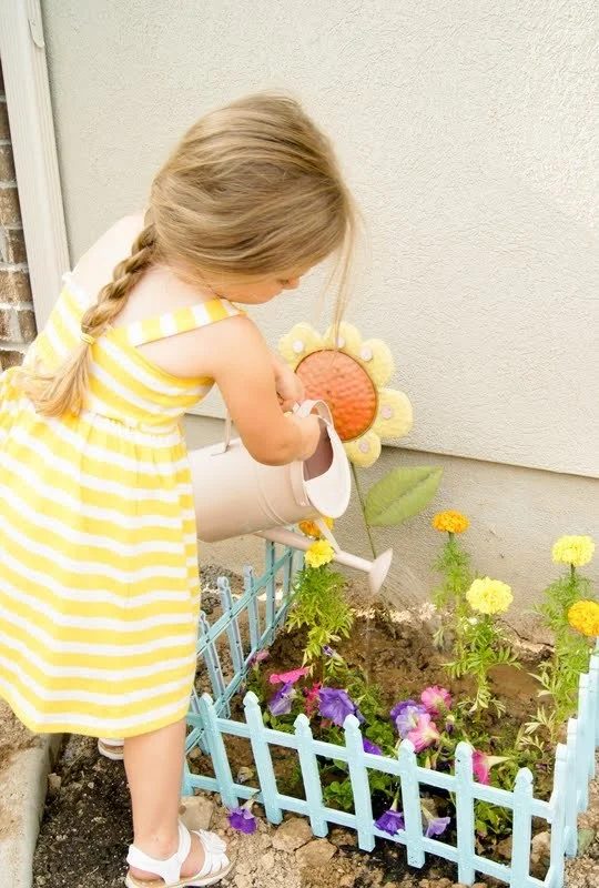 Gardening With Kids, Little Girl In Yellow And White Striped Sun Dress Watering A Flower Garden