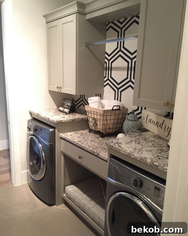 Modern washroom with front loading washer and dryer, stylish counter space, drawers, cupboard, hanging rod, and accent wall with patterned wallpaper.