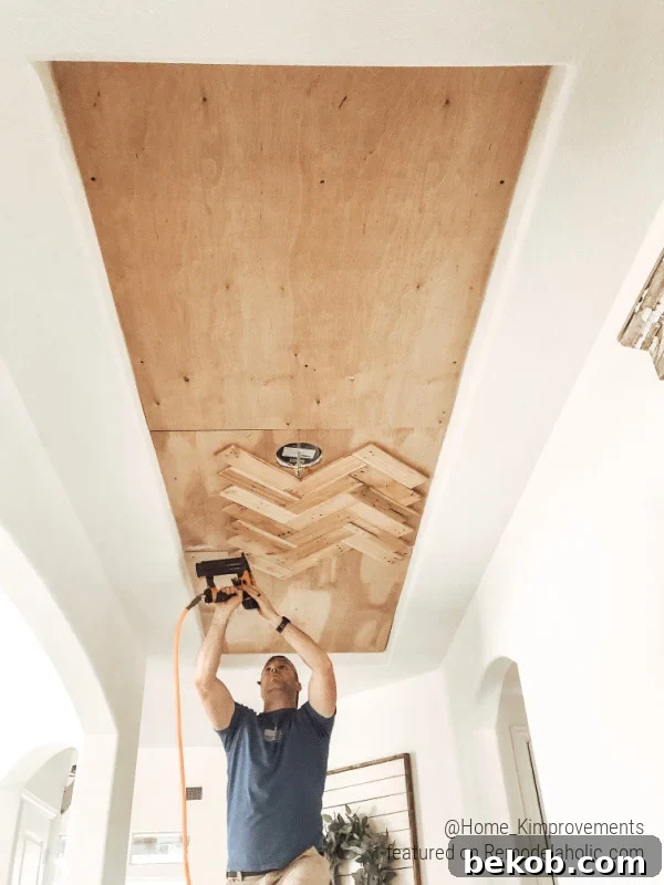 Installing pallet wood slats in a herringbone pattern on a tray ceiling inset, demonstrating the DIY process for a modern farmhouse entry.
