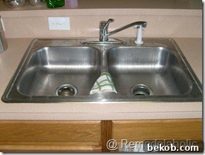 Close-up of the original kitchen's cheap faucet and shallow sink, showing grime and poor functionality.