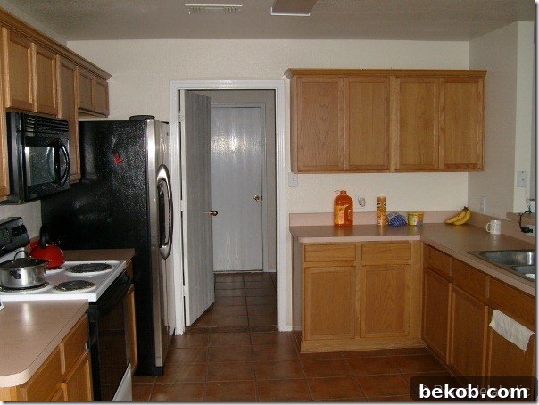 View of the original kitchen looking into the laundry room and towards the garage door, showing the existing floor tile and overall kitchen configuration.