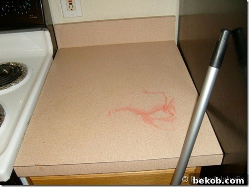 A peachy-pink kitchen countertop heavily stained with red Kool-Aid, showcasing significant wear and tear.