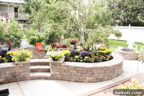 Retaining wall and fire pit kit defining an outdoor space, with beautiful fall flowers planted nearby.