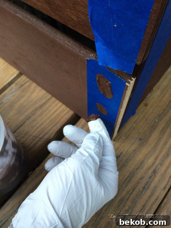 Smart tip for hiding nail holes in stained wood! This image demonstrates the process of filling nail holes with stained wood putty and removing painter's tape for a clean finish.