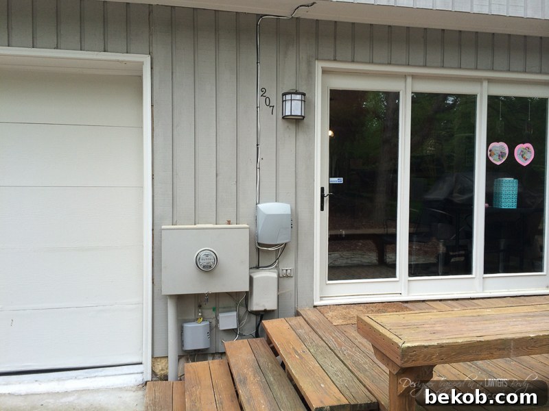 Before - DIY utility box cover. This image shows the unsightly utility boxes and wires on the side of a house before any concealment, highlighting the need for an aesthetic solution.
