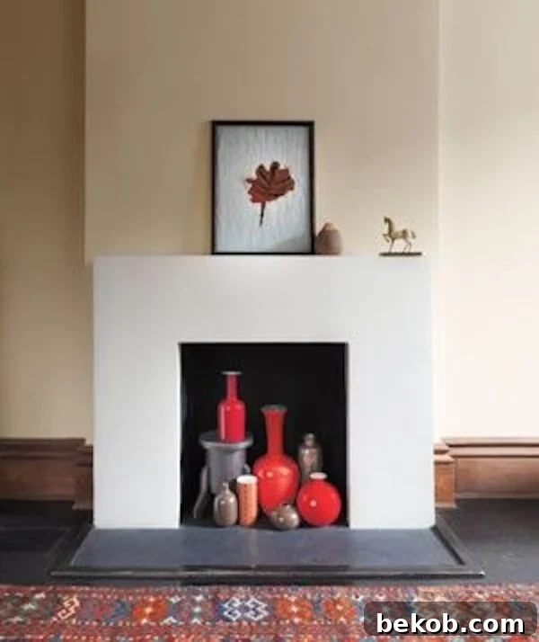 Beautifully styled non-functional fireplace with vibrant red vases and framed art