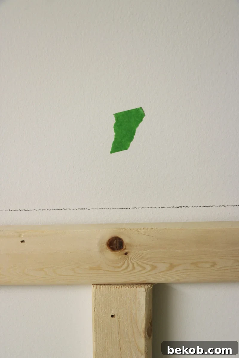 Marking the positions of wall studs above the installed pegboard for precise screw placement.